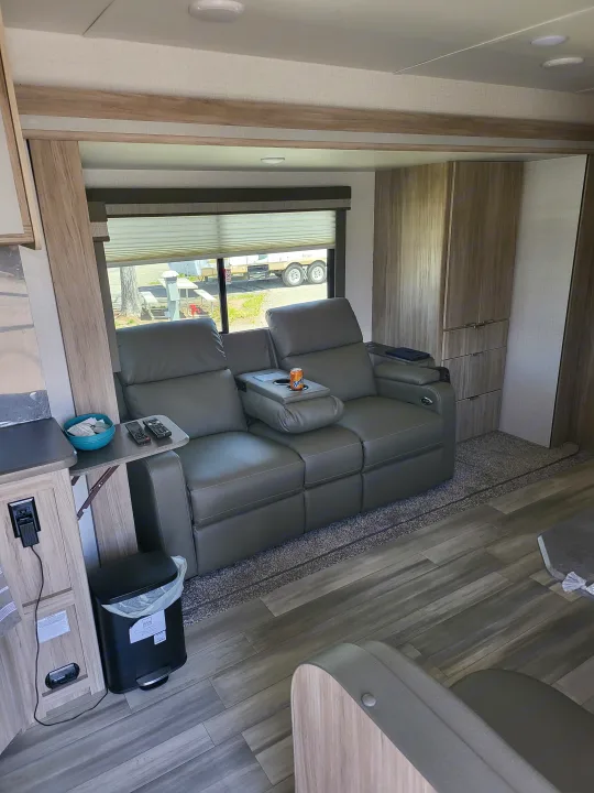 Step inside a spacious RV rental. This modern living area boasts a comfy grey sectional with cupholders, wood-look flooring, and ample light.. Winnebago Minnie Winnie 2022