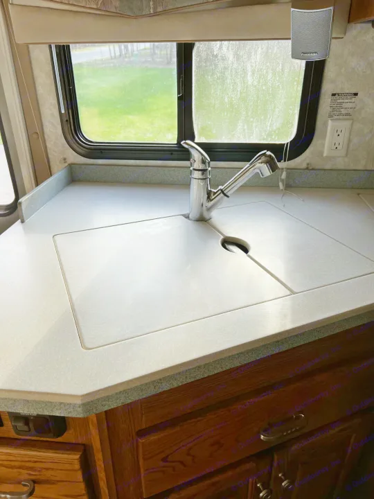 Inside an RV rental, featuring a compact kitchen counter with a pull-out faucet, covered sink, and scenic window view.. Allegro Allegro Bay 2004