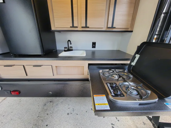 This rv rental offers a compact kitchen area with a sink, fridge, and cabinets. A pull-out Flame King outdoor stove extends for cooking.. Cruiser Rv Corp Radiance 30ds 2021