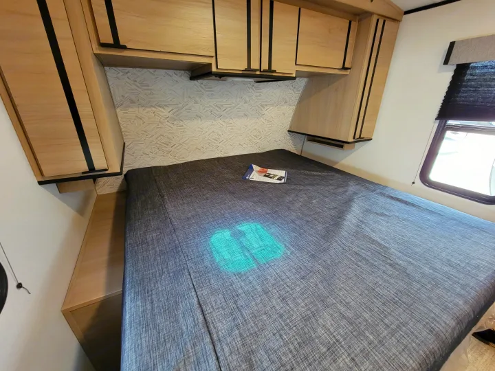 RV rental interior featuring a bedroom with a patterned headboard wall, bed, and light wood overhead storage.. Cruiser Rv Corp Radiance 30ds 2021