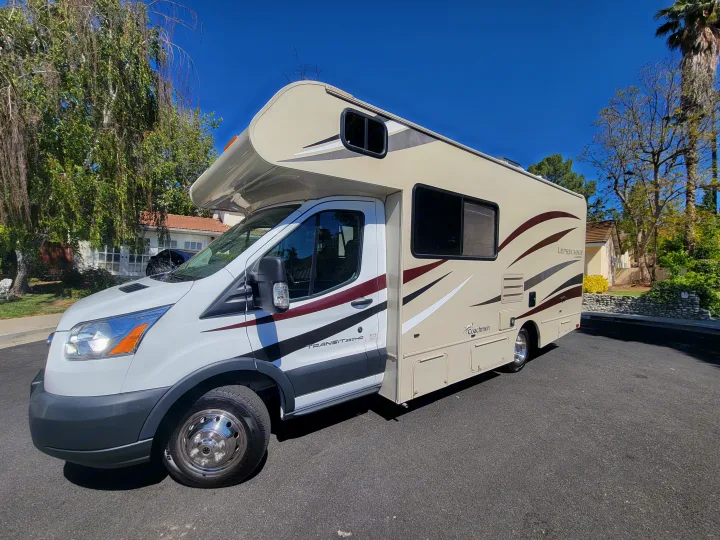 A large, beige Class C RV, a Coachmen Leprechaun, sits on an asphalt street. Perfect for your next rv rental adventure.. Coachman Leprechaun 2018