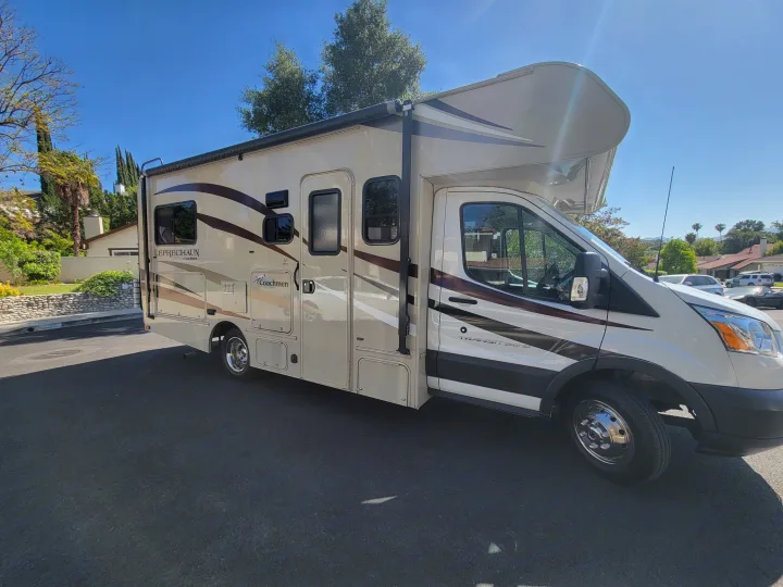 Beige & brown Coachmen Leprechaun motorhome RV rental, parked on a sunny residential street.. Coachman Leprechaun 2018