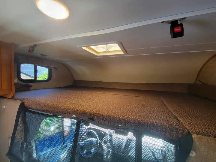 Cozy cab-over bunk in an RV rental, featuring a spacious sleeping area, window, light, vent, and safety mesh.. Coachman Leprechaun 2018