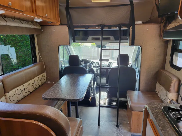 Spacious RV rental interior featuring a dinette, kitchen, and ladder to an overhead bunk.. Coachman Leprechaun 2018