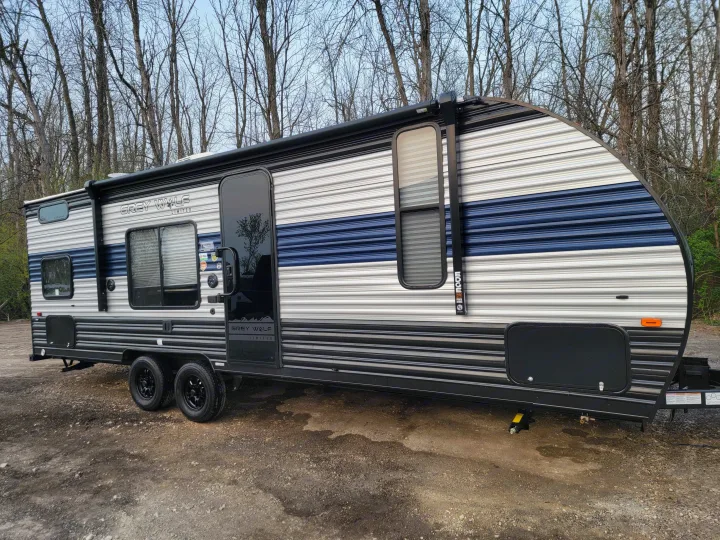A modern Grey Wolf travel trailer with blue and grey stripes, ideal for RV rental, parked on gravel.. Forest River Cherokee Grey Wolf 2022