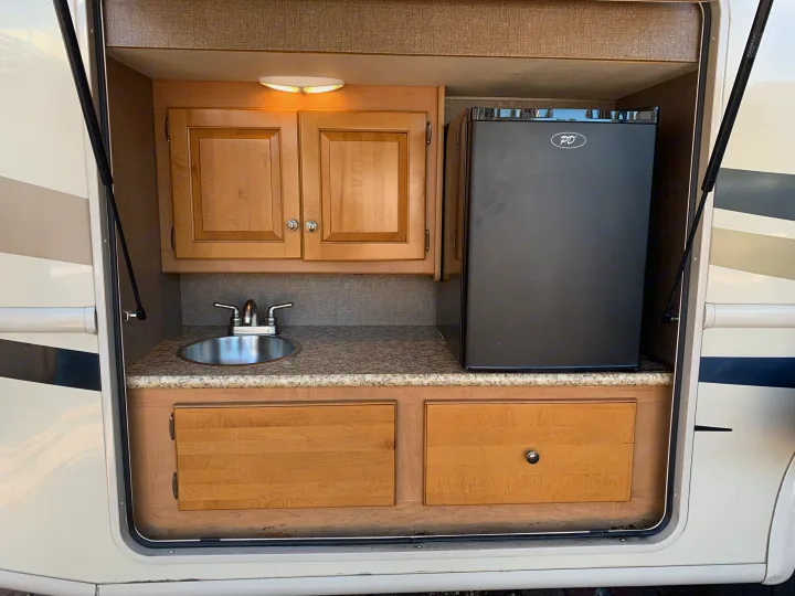Convenient outdoor kitchen in an RV rental, equipped with a sink, mini-fridge, and overhead cabinets for trips.. Thor Windsport 2017