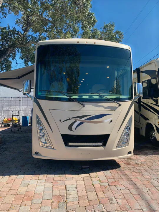 Front view of a cream RV rental, parked on brick pavers under a tree. Another RV is partially seen beside it.. Thor Windsport 2017
