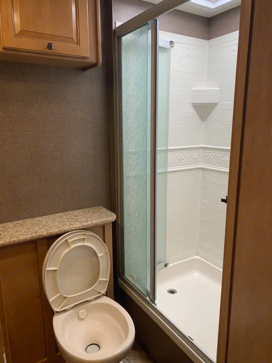 Clean and compact RV rental bathroom with a toilet, overhead cabinet, and a shower featuring a glass door. Functional for travel.. Thor Windsport 2017