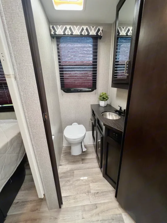 Step inside this modern RV rental featuring a clean bathroom with a toilet, sink vanity, and window with blinds.. Entegra Coach Odyssey 2021
