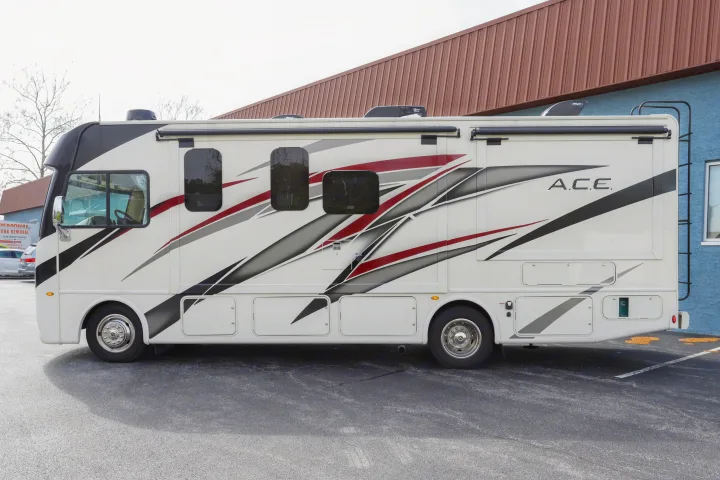 A white motorhome RV rental, featuring black, gray, and red graphics on its side, parked on asphalt.. Thor Motor Coach A.C.E 2022