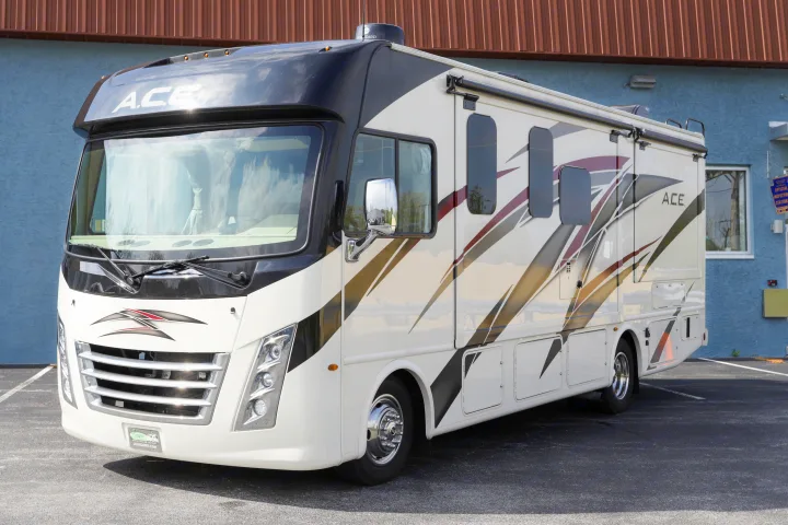 This white Thor ACE Class A motorhome, ideal for rv rental, is parked on asphalt with a blue building backdrop.. Thor Motor Coach A.C.E 2022