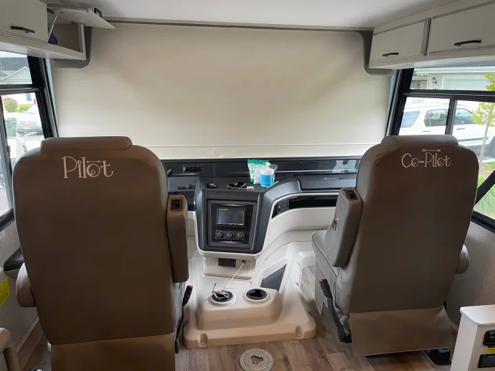 Inside an RV rental: Front cabin with "Pilot" and "Co-Pilot" seats, dashboard controls, and bright windows.. Jayco Precept 2021