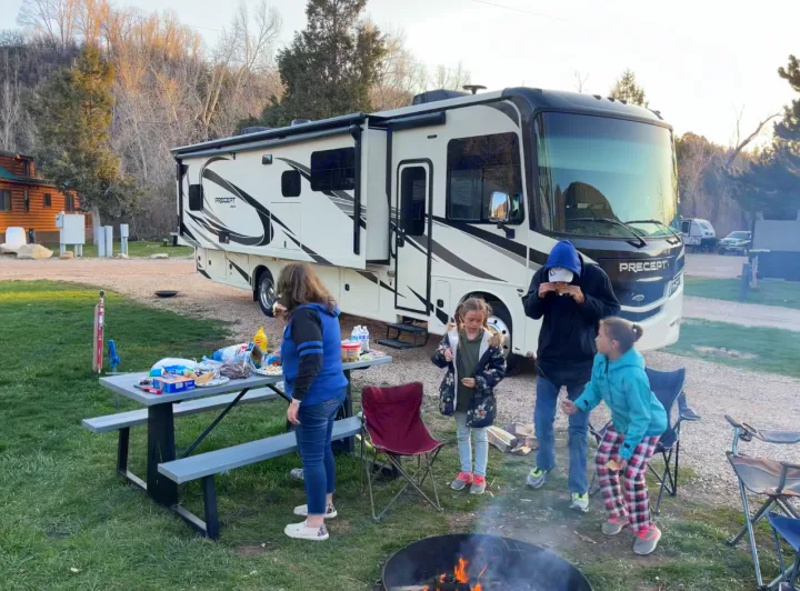 Family camping trip! Enjoying a campfire and snacks by their spacious RV rental at a scenic campground. Great outdoor memories.. Jayco Precept 2021