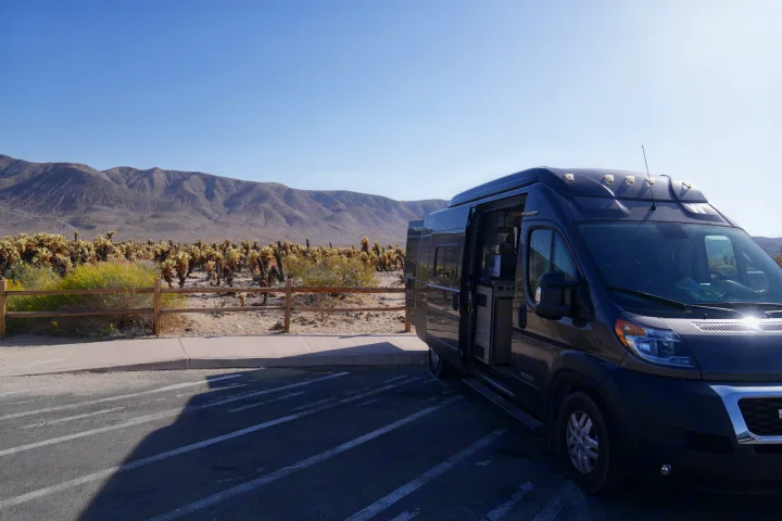 Dark grey RV rental van parked by a cholla cactus garden with mountains under a clear blue sky.. Winnebago Solis 2022