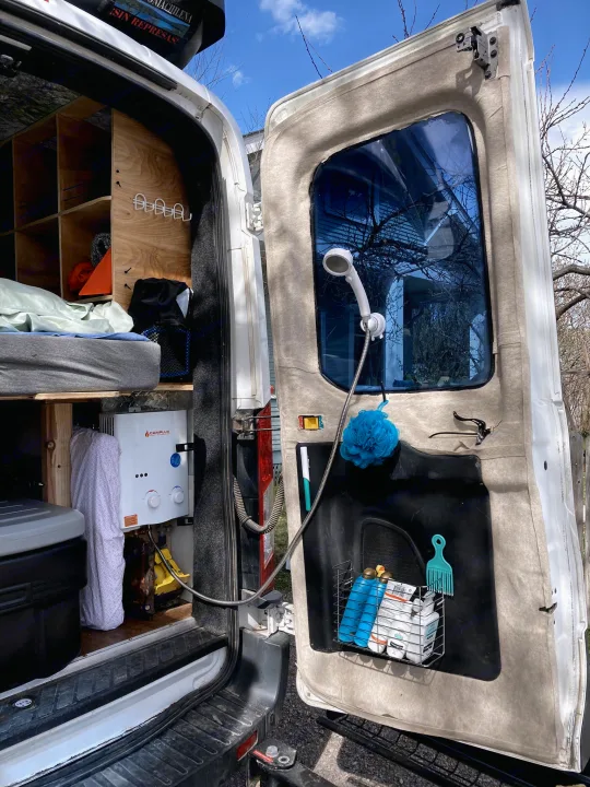 RV rental features: an outdoor shower from the back of the van, with a water heater, shower head, and toiletries visible.. Ford Transit Custom 2015