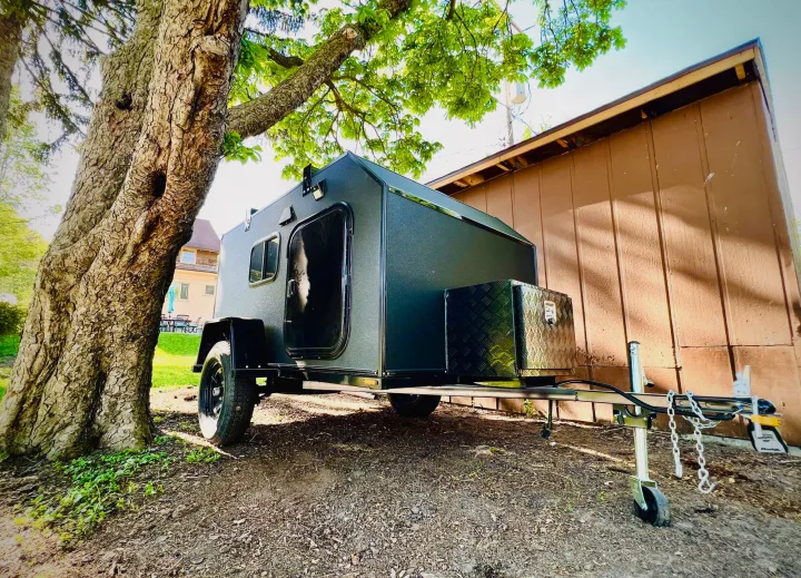 Sleek, dark gray teardrop camper parked under a tree. This compact rv rental is perfect for outdoor travel & camping.. Other Other 2022
