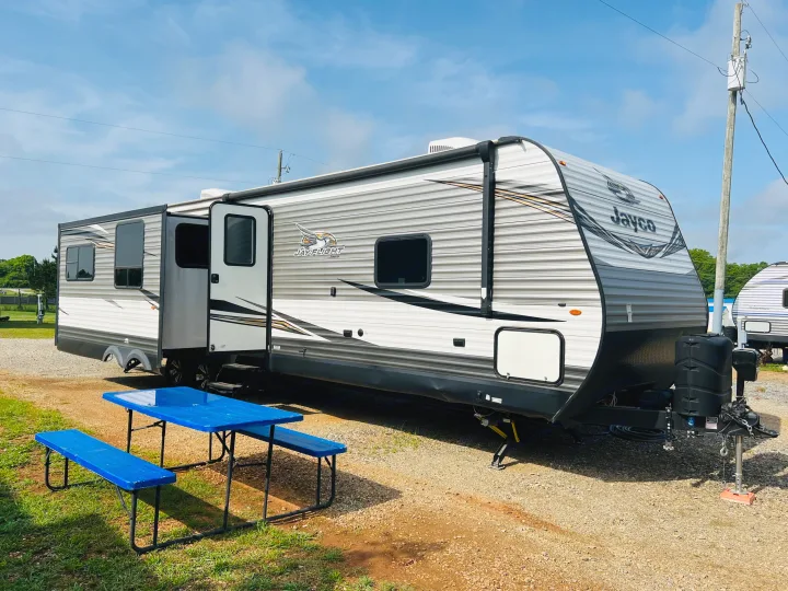 Spacious Jayco travel trailer RV rental at a sunny campsite with a blue picnic table, ready for your next adventure.. Jayco Jay Flight 2019