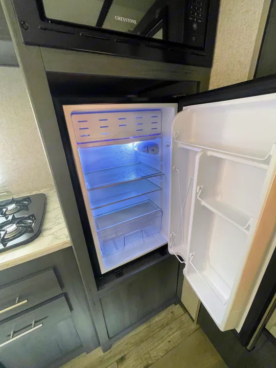 RV rental kitchen featuring a compact, empty refrigerator, Greystone microwave, and stovetop, perfect for your journey.. Dutchmen Aspen Trail 2021
