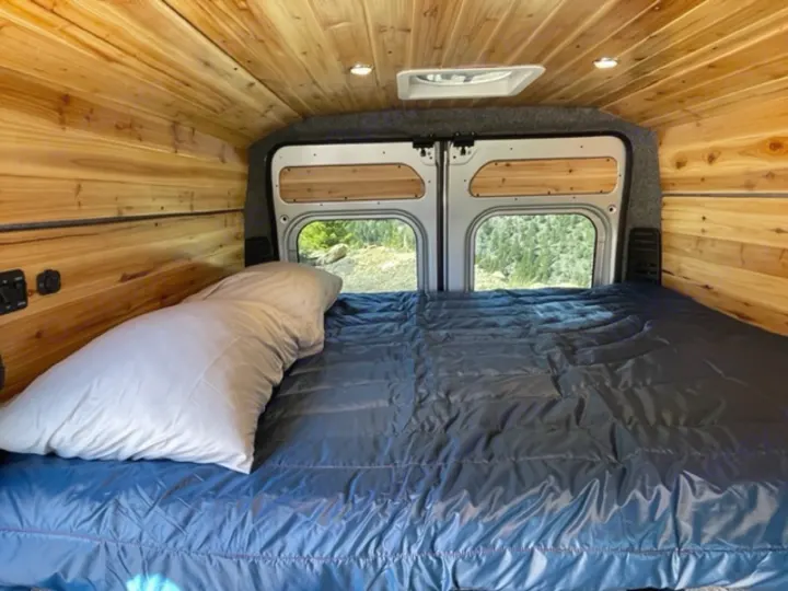 Cozy RV rental bedroom with wood paneling, a comfy bed, and a scenic view out the back windows.. RAM Promaster ALPINE X Edition OA15 2021