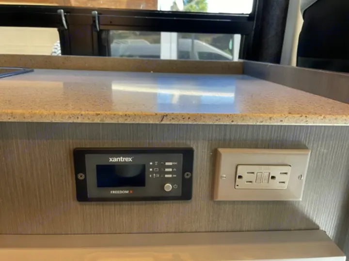 RV rental kitchen showing a Xantrex Freedom X inverter control panel and a GFCI electrical outlet under a speckled countertop.. RAM Promaster ALPINE X Edition OA15 2021