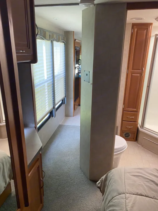Inside our RV rental: a practical layout showing the bedroom, carpeted hallway, and a compact bathroom with toilet and shower.. Fleetwood Jamboree 2005