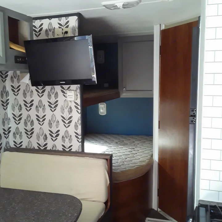RV rental interior showcasing a modern dinette area with TV, overhead storage, and a peek into the bedroom.. Heartland RVs Trail Runner 2013