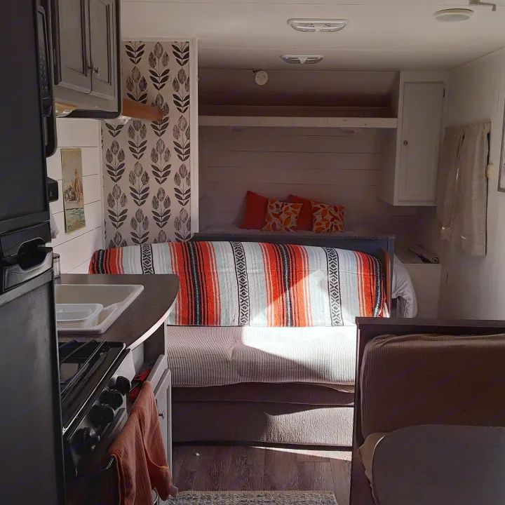 Warm RV rental interior showing a compact kitchen, colorful bed, and bunk for cozy travel living.. Heartland RVs Trail Runner 2013