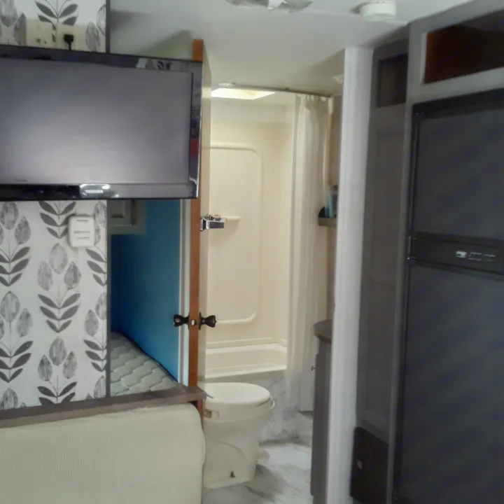 RV rental interior: compact space with overhead storage, a monitor, toilet, and patterned wall visible.. Heartland RVs Trail Runner 2013