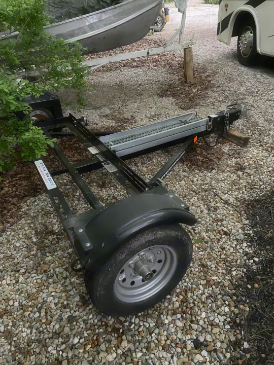 RV rental journey ready: A boat on its trailer, a car tow dolly, and a white RV on a gravel driveway.. Acme Tow Dolly Company Two Wheel Dolly 2016