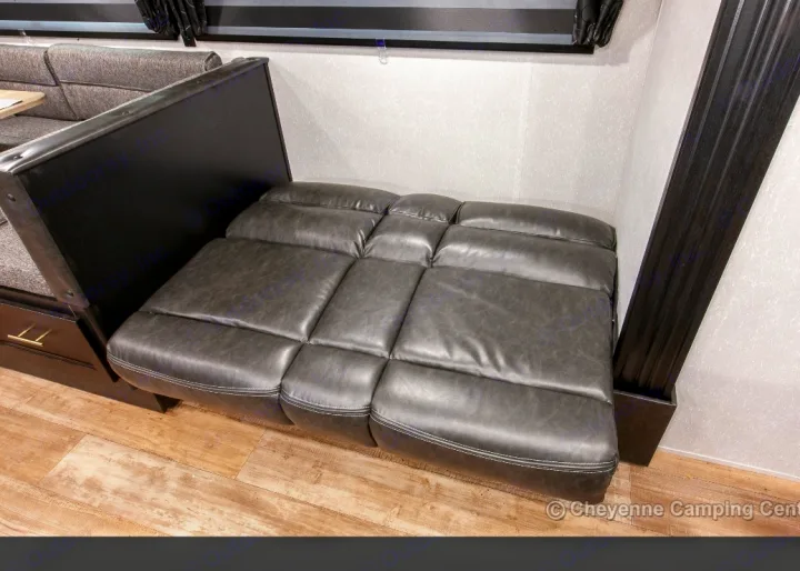 RV rental interior with a grey faux-leather sectional sofa converted into a bed. Features include a nearby dinette & wood-look floor.. Forest River Cherokee Grey Wolf 2022