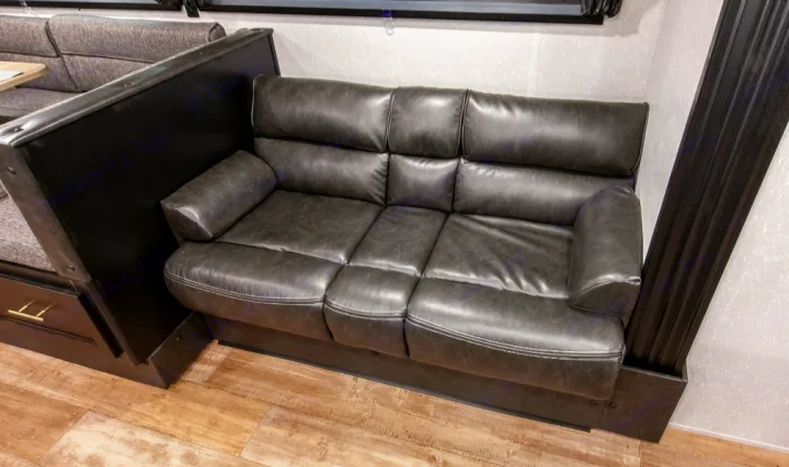 Dark gray faux leather sofa and dinette in an RV rental interior. Comfortable camper living space.. Forest River Cherokee Grey Wolf 2022