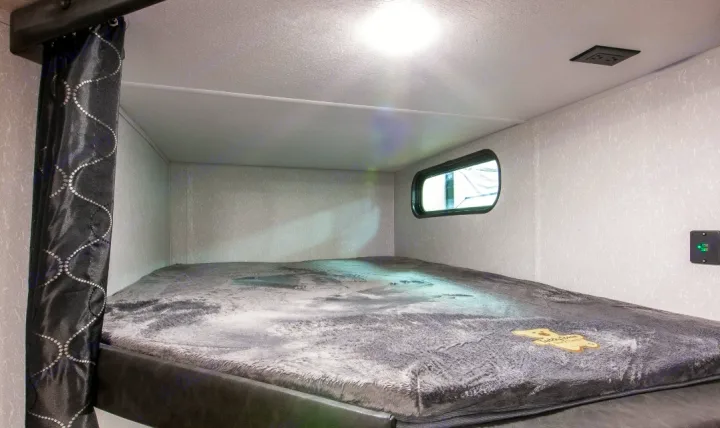 Explore this cozy bunk sleeping area inside an RV rental, featuring a soft blanket, window, and power outlets.. Forest River Cherokee Grey Wolf 2022