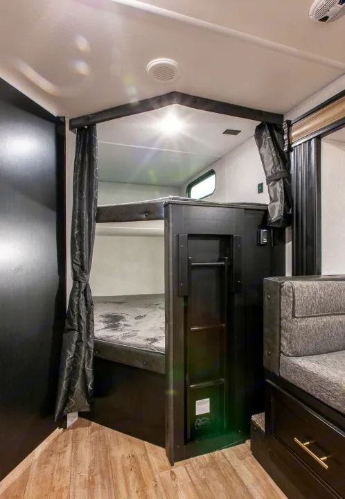 Compact RV rental interior featuring dark bunk beds, a small seating area, and wooden flooring, ideal for family travel.. Forest River Cherokee Grey Wolf 2022