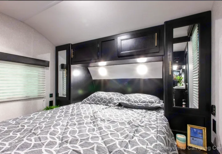 Modern rv rental bedroom with grey patterned bedding, black overhead cabinets, and built-in lighting. Compact and cozy interior.. Forest River Cherokee Grey Wolf 2022