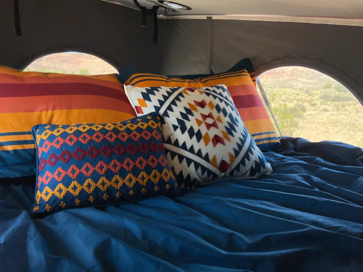 Cozy bed in an RV rental, featuring vibrant southwestern pillows, blue sheets, and a serene desert view.. Winnebago Solis 2022