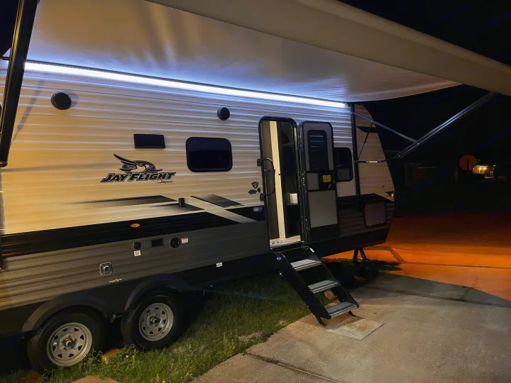 Experience an rv rental! This illuminated Jayco travel trailer with open awning and steps is set up at night, ready for your trip.. Jayco Jay Flight 2022