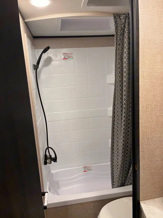 Compact RV rental bathroom with a white shower/tub, black handheld showerhead, and a gray geometric shower curtain.. Jayco Jay Flight 2022