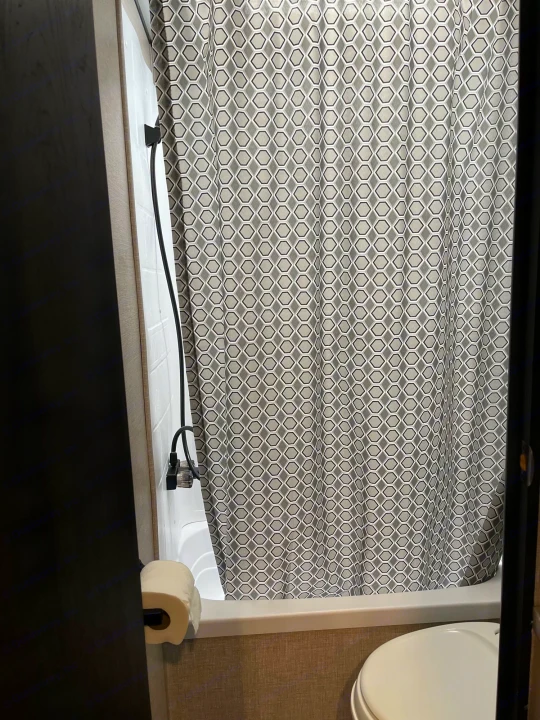 Compact RV rental bathroom featuring a patterned shower curtain, flexible showerhead, and toilet.. Jayco Jay Flight 2022