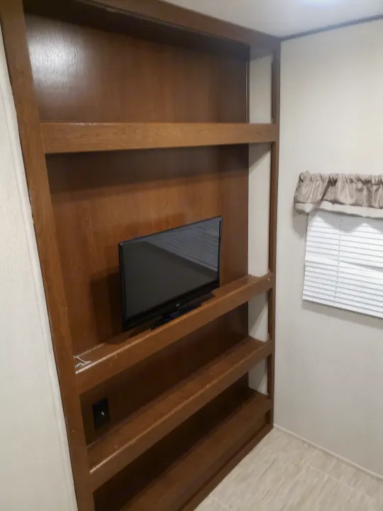 RV rental: Integrated wooden shelving unit with a TV and a window with blinds, optimizing space for comfort.. Avenger ATI 2020