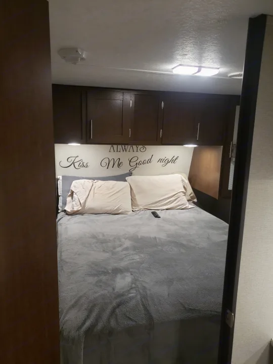 Cozy RV rental bedroom with a comfortable bed, overhead cabinets, and a decorative headboard sign.. Avenger ATI 2020