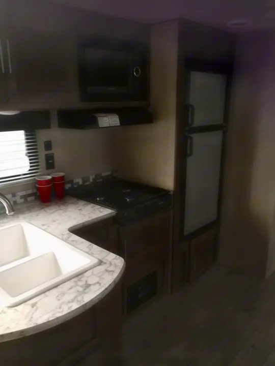 Compact RV rental kitchen with sink, stovetop, microwave, and refrigerator, perfect for travel.. Grand river 32bhs 2019