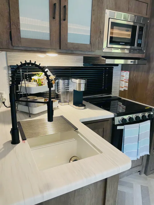 Modern RV rental kitchen featuring a sleek sink, black faucet, built-in microwave, and oven/stove combo.. Forest River Salem 2022