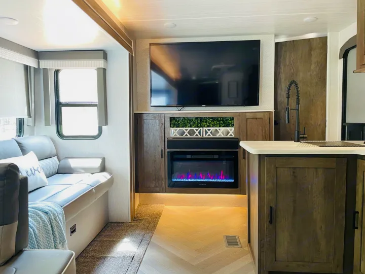 Cozy RV rental interior: Living room with a large TV, electric fireplace, comfortable sofa, and kitchen sink.. Forest River Salem 2022