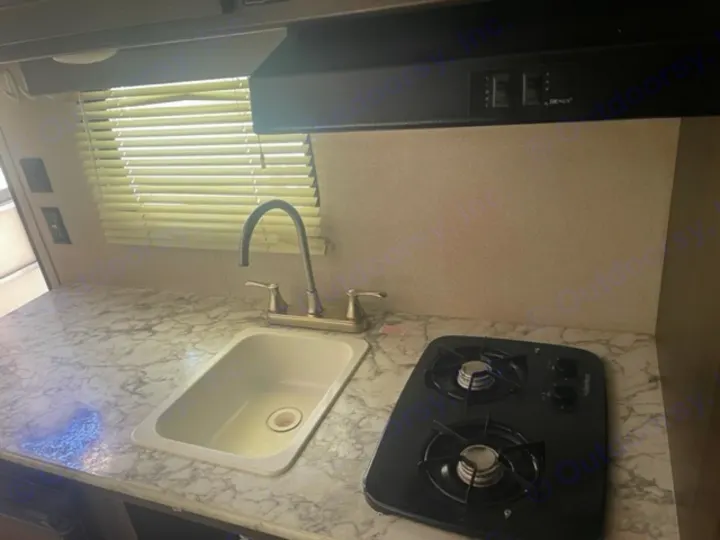 Inside an RV rental, this functional kitchen features a sink, two-burner stovetop, and marble-look counter, perfect for travel.. Keystone RV Springdale 2019