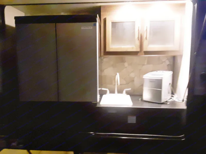 Well-lit RV rental kitchenette featuring a compact fridge, sink, ice maker, and overhead storage cabinets.. Forest River Cherokee Grey Wolf 2020