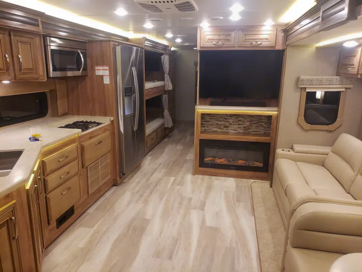 Modern rv rental interior showing kitchen with stove/microwave, bunk beds, and living space with TV, fireplace, and sofa.. Jayco Seneca 37L 2021