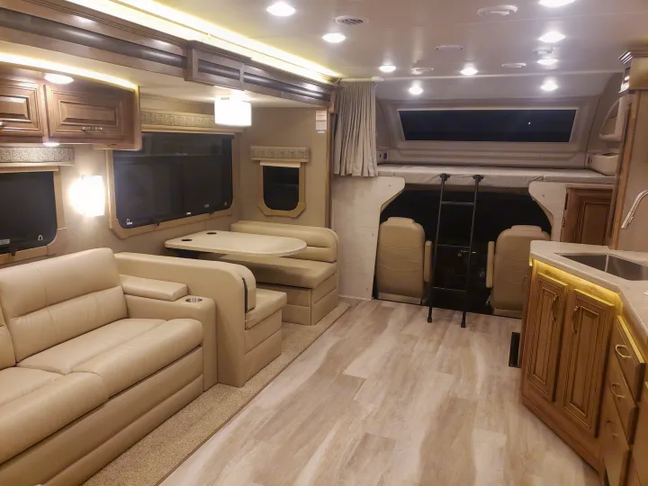 Spacious RV rental interior with living, dining, kitchen areas, over-cab bunk bed, and bright modern lighting.. Jayco Seneca 37L 2021
