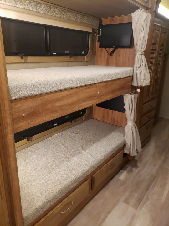RV rental: stacked bunk beds with light mattresses, personal TVs, and storage cabinets.. Jayco Seneca 37L 2021