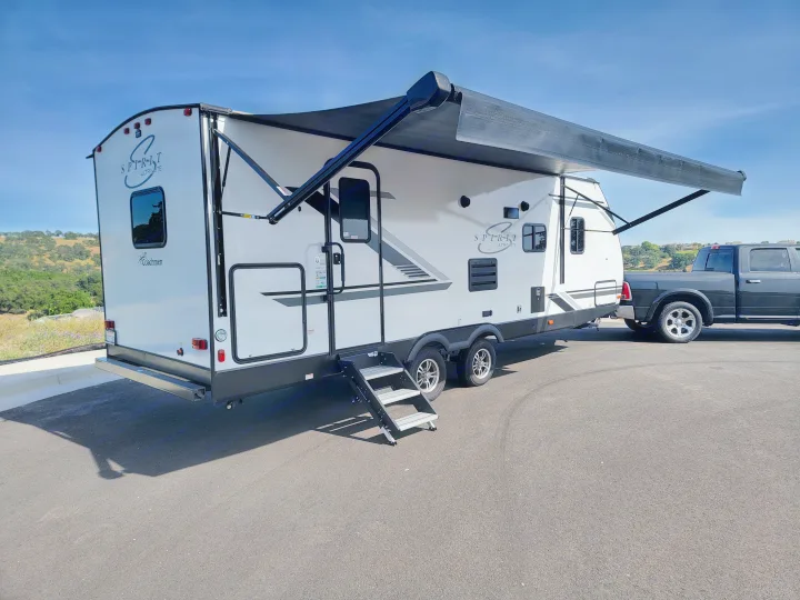 A white Coachmen Spirit Ultra Lite travel trailer with its awning extended, hitched to a pickup. Ideal for rv rental.. Coachmen Spirit Ultra Lite 2021