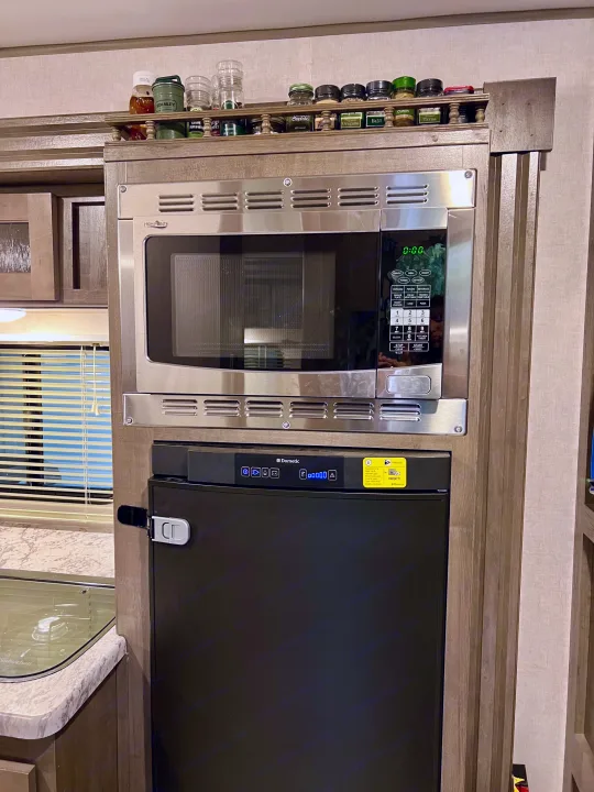 This RV rental kitchen features a compact High Pointe microwave over a Dometic refrigerator, with spices overhead.. R-Pod Hood River Edition 2017